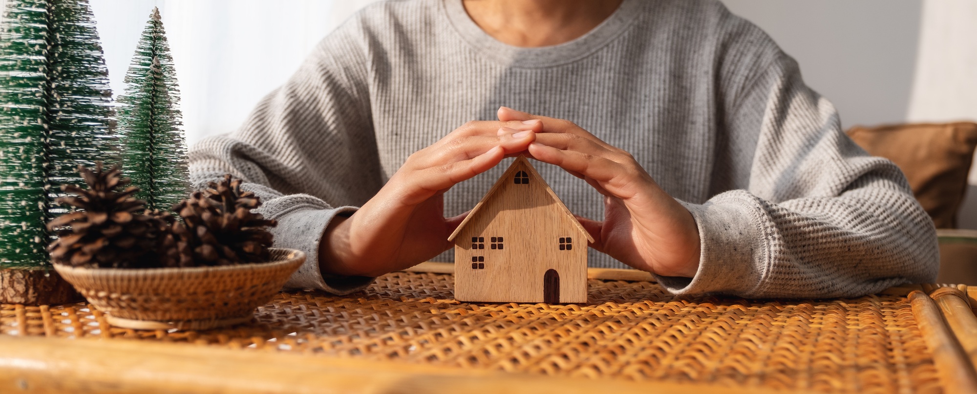 Closeup image of a woman protecting and covering wooden house model by hands with warmness